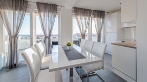 A modern, well-lit room with a dining table, white chairs, and a view of the city through large windows. - Villa Magnifica Apartments with pool (Novalja)