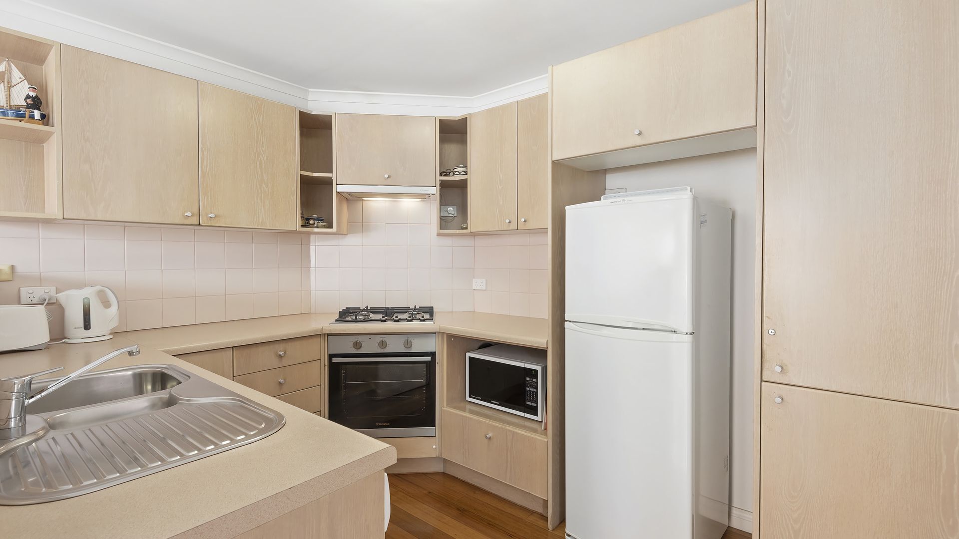 A compact kitchen with wooden cabinets, a built-in oven, a microwave, and a refrigerator.