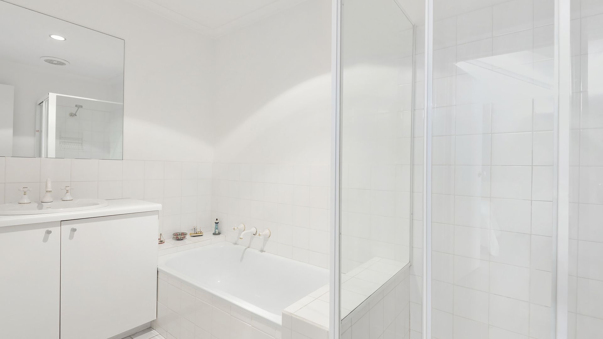 Un bany modern amb un lavabo blanc, una banyera i un espai de dutxa amb envàs de vidre.
