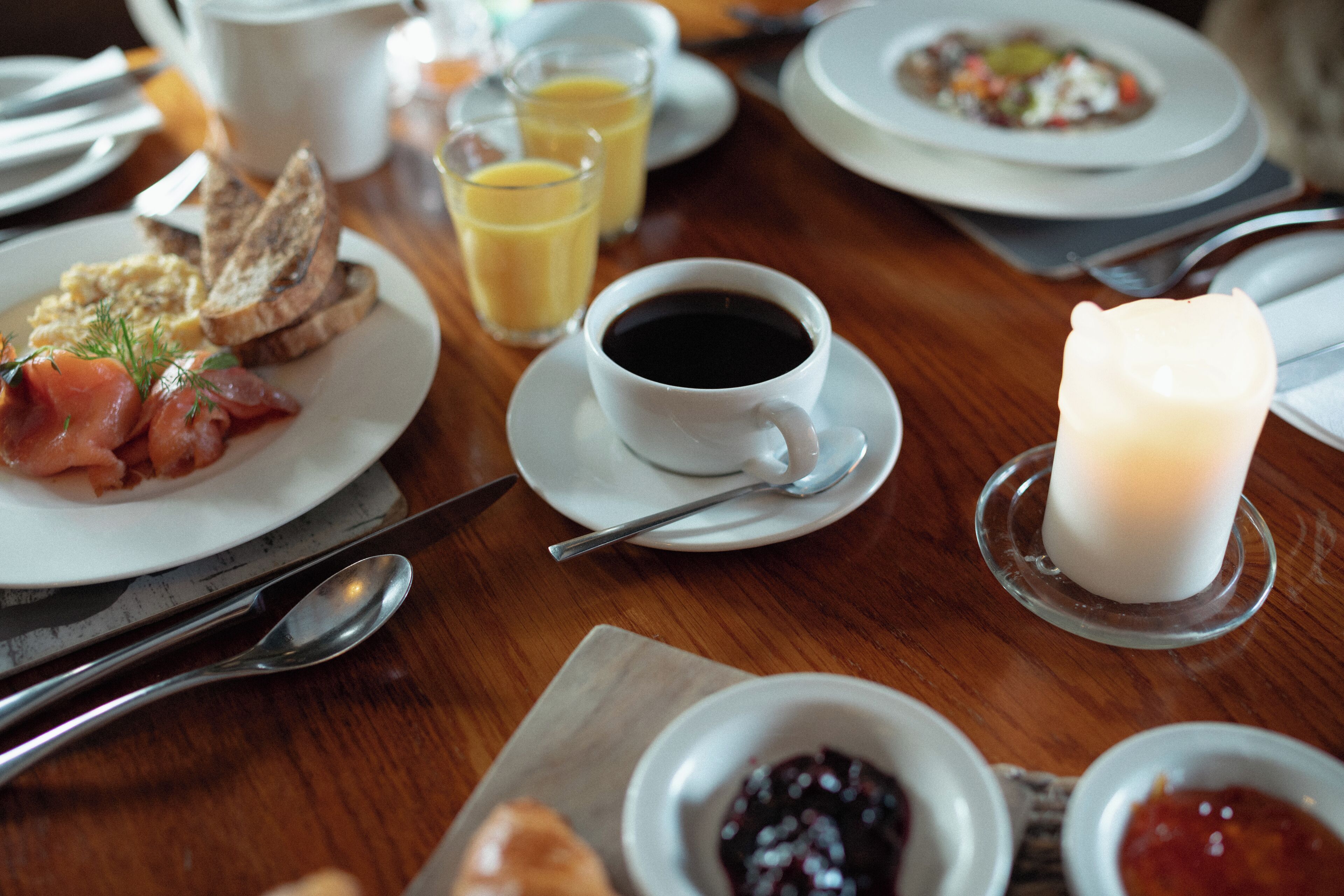 Ein Frühstückstisch mit Speisen, einer Kaffeetasse und einer Kerze auf einer Holztischplatte.