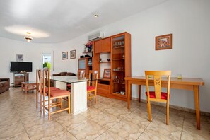 A living room with a TV, dining table, chairs, and a cabinet with glassware.