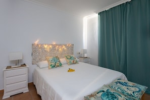 A bedroom with a bed, two bedside tables, a decorative headboard, and a window with curtains.