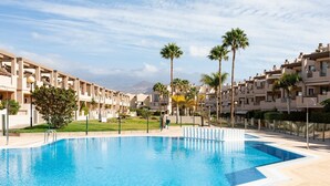 Una piscina circondata da edifici a più piani con balconi, cielo sereno e palme.