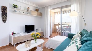 Un soggiorno moderno con televisione, arredi bianchi, un balcone con tavolo e sedie e vista esterna.