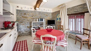 A dining area with a stone wall, a red tablecloth, white chairs, and a television. - Holiday Home "Casa dei Tigli" with Mountain View, Garden & Wi-Fi (Ormea)