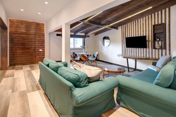 A modern living room with a sectional sofa, a dining table with chairs, a TV mounted on a wooden wall, and a wooden door. - Vacation Home "Casa Miranda" with Whirlpool & Wi-Fi (Candelaria)