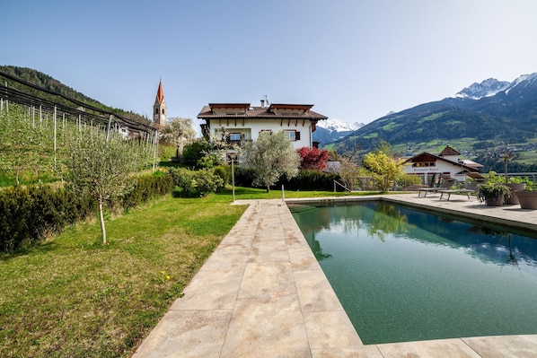 Une maison avec une piscine, entourée de verdure et de montagnes.