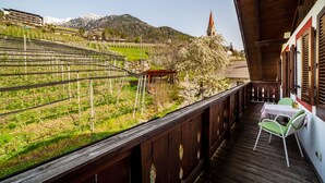 A balcony with a table and chairs, a vineyard view, and a mountain backdrop.