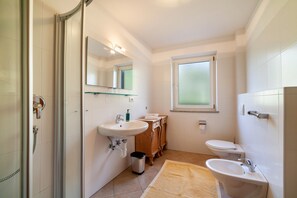 Et badeværelse med brusekabine i glas, vask, toilet og et spejlskab.