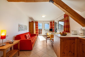 A cozy living area with a red sofa, wooden dining table, and kitchen counter.