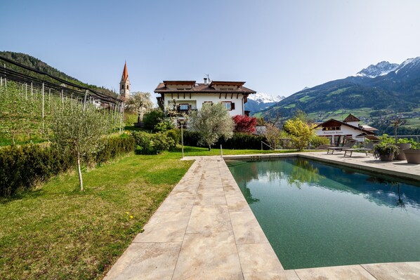 A house with a pool, surrounded by greenery and mountains.
