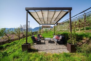 A covered outdoor seating area with a pergola, a sofa, two chairs, and a table.