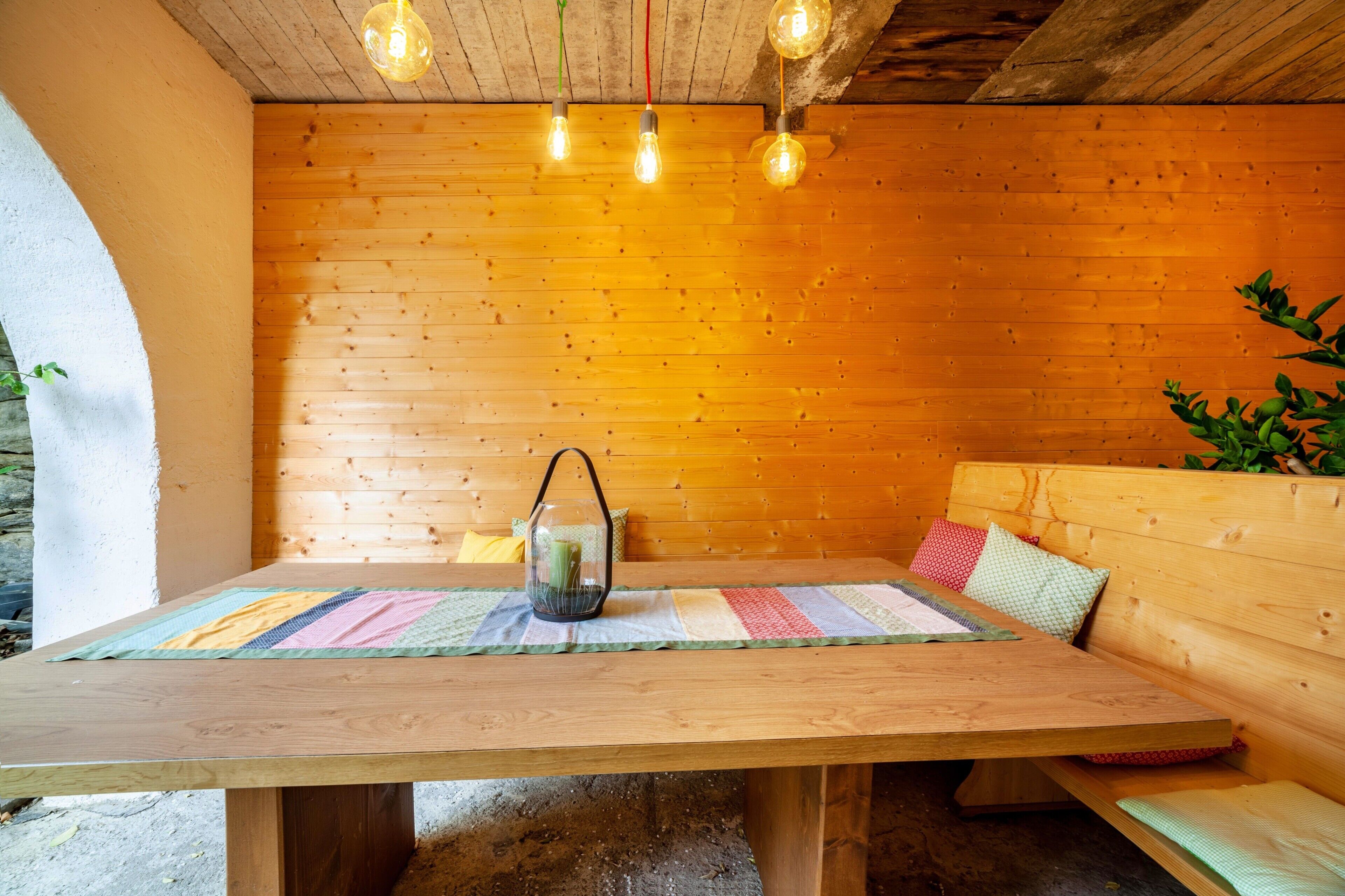 A wooden table with a colorful placemat, a glass lantern, and a bench with cushions.