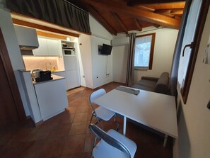 Une cuisine compacte avec un coin repas, un téléviseur à écran plat fixé au mur et une fenêtre avec des rideaux.