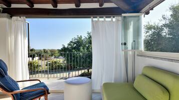 Un balcone con una sedia, un divano e una porta vetrata che dà su alberi e un recinto.