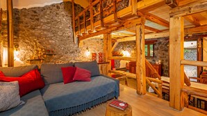 Une pièce chaleureuse avec un plafond en bois, des murs en pierre, un canapé avec des coussins rouges et une table en bois.