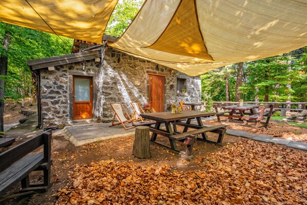 A rustic stone building with a wooden door, a picnic table, and benches.