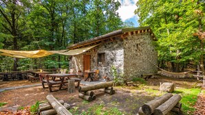 Un chalet rustique en pierre avec une terrasse en bois, des tables de pique-nique et un hamac.