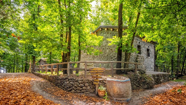 Un bâtiment en pierre avec un pont en bois, entouré d’arbres et d’un mur de pierre.