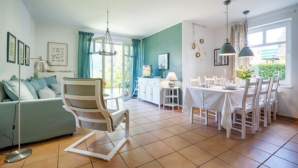 Amplia sala de estar con sofá, una mesa de comedor lista para cuatro personas y una silla.
