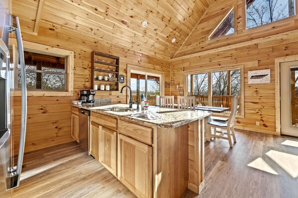 Une cuisine rustique, située dans une cabane en bois, avec un grand îlot central, des armoires en bois et un réfrigérateur.