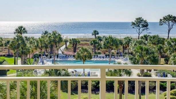 A pool area with lounge chairs and palm trees, overlooking a beach and ocean. - 433 Shorewood: 2 Bedroom Ocean View Villa, Free Bikes, Beach Chairs (Hilton Head Island)