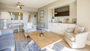 A living room with a wooden coffee table, a sofa, a chair, and a TV mounted on the wall. - 433 Shorewood: 2 Bedroom Ocean View Villa, Free Bikes, Beach Chairs (Hilton Head Island)