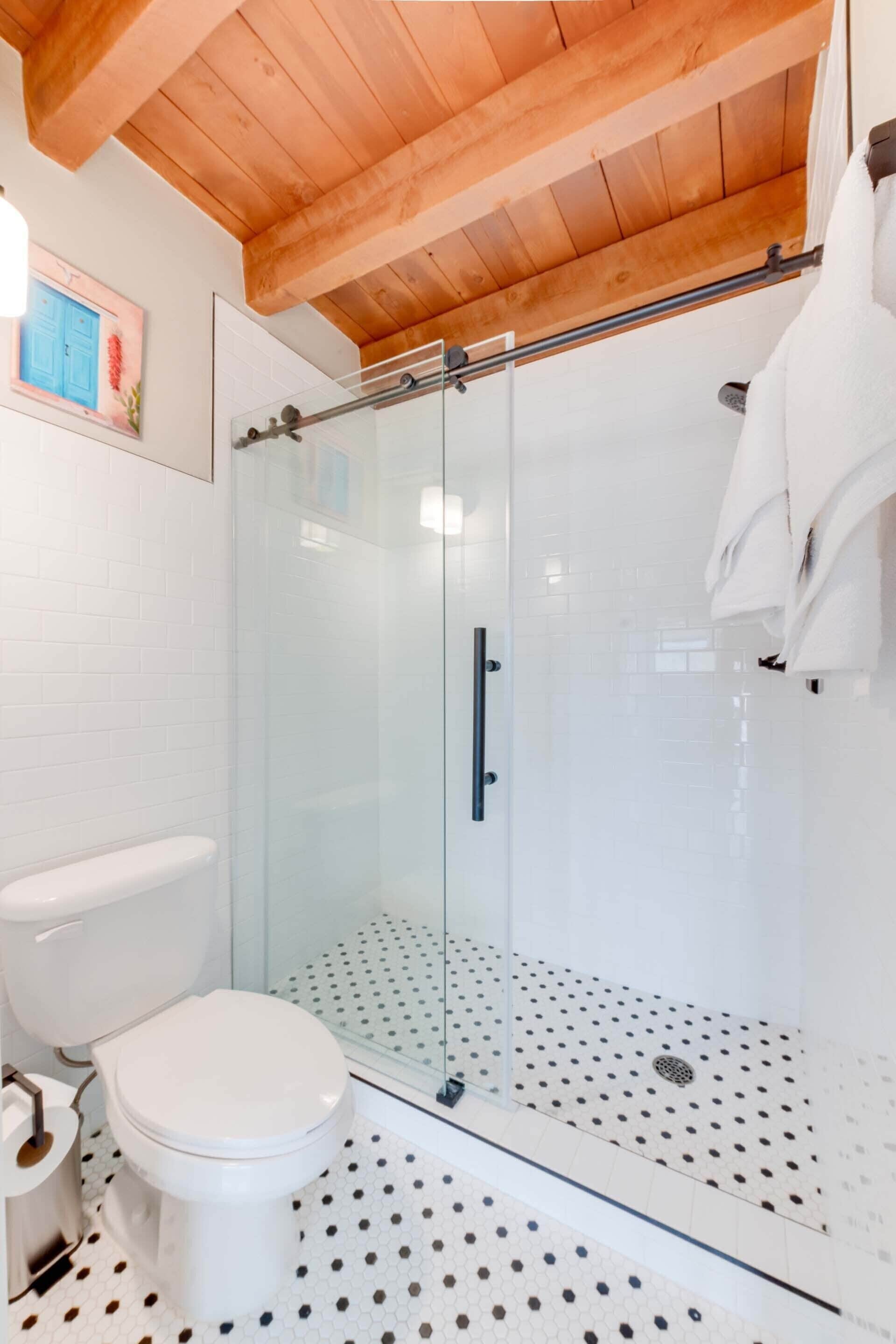A modern bathroom with a glass-enclosed shower, white tiles, and a wooden ceiling.