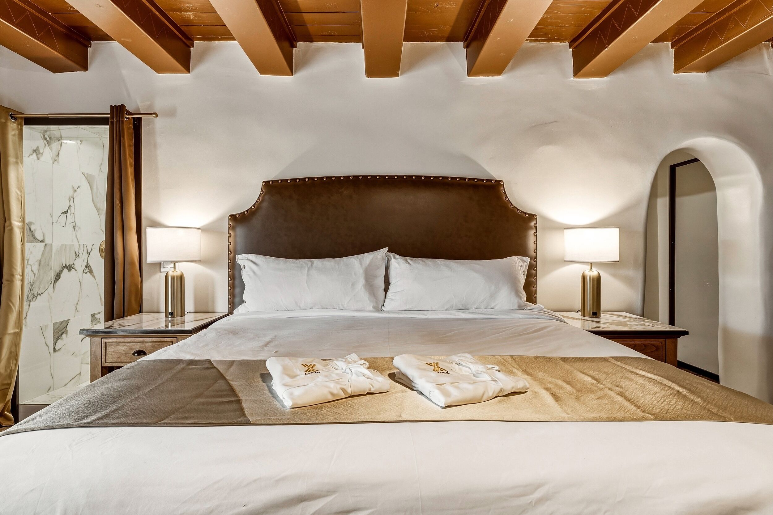 A hotel room with a large bed, two bedside lamps, a marble-patterned wall, and an arched mirror.