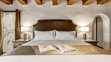 A hotel room with a large bed, two bedside lamps, a marble-patterned wall, and an arched mirror.