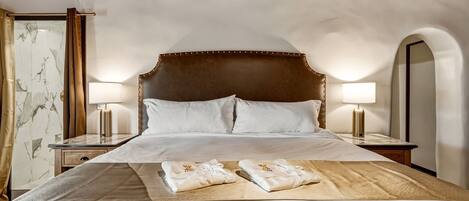A hotel room with a large bed, two bedside lamps, a marble-patterned wall, and an arched mirror.
