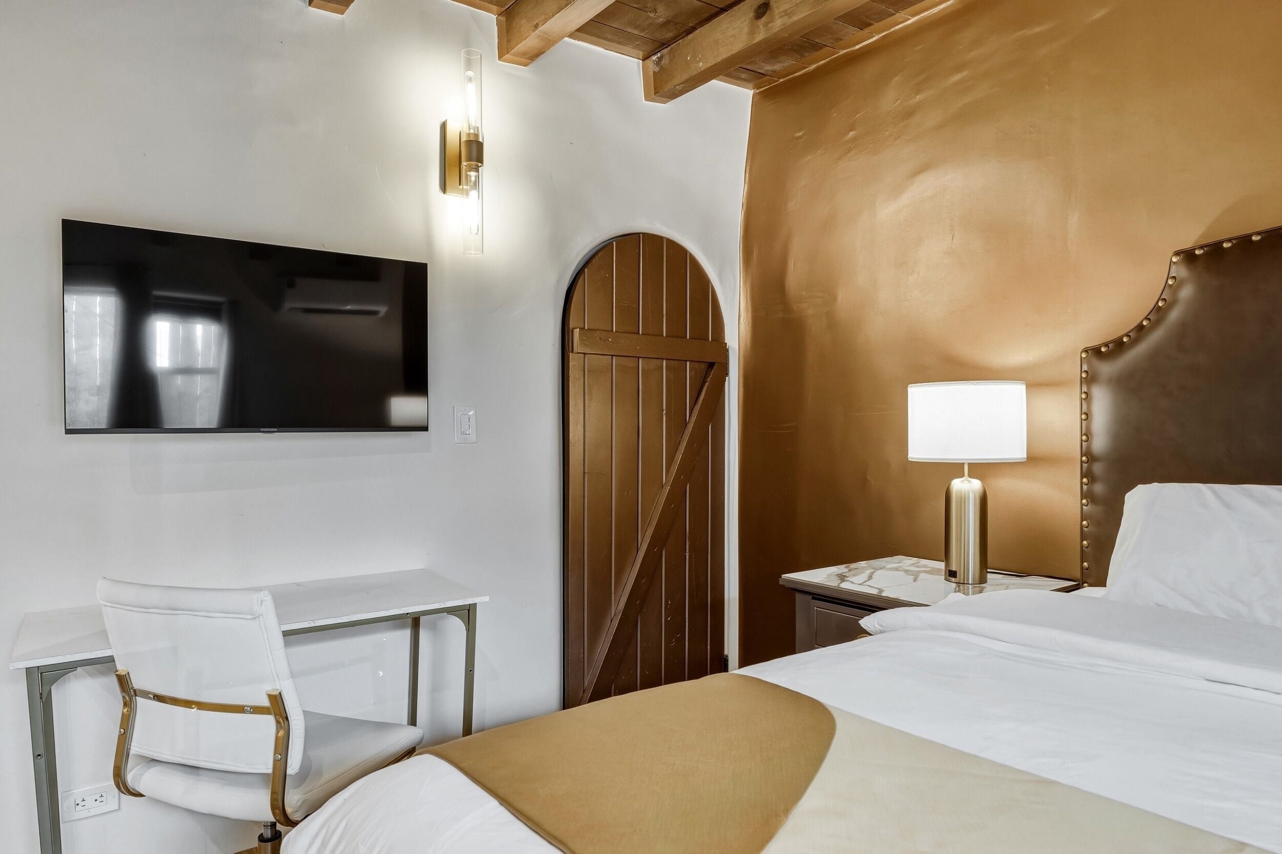 A hotel room with a bed, a desk, a chair, a television, and a nightstand with a lamp.