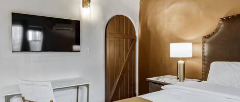 A hotel room with a bed, a desk, a chair, a television, and a nightstand with a lamp.
