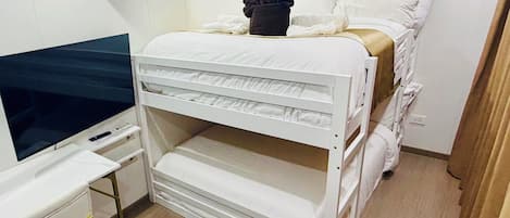 A compact hotel room with a bunk bed, a desk with a flat-screen TV, and a wall-mounted air conditioner.