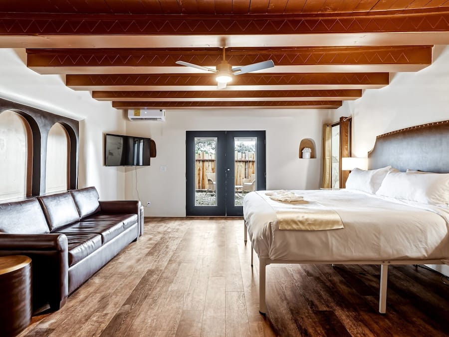 A bedroom with a bed, a sofa, a TV, and a door leading to an outdoor area.