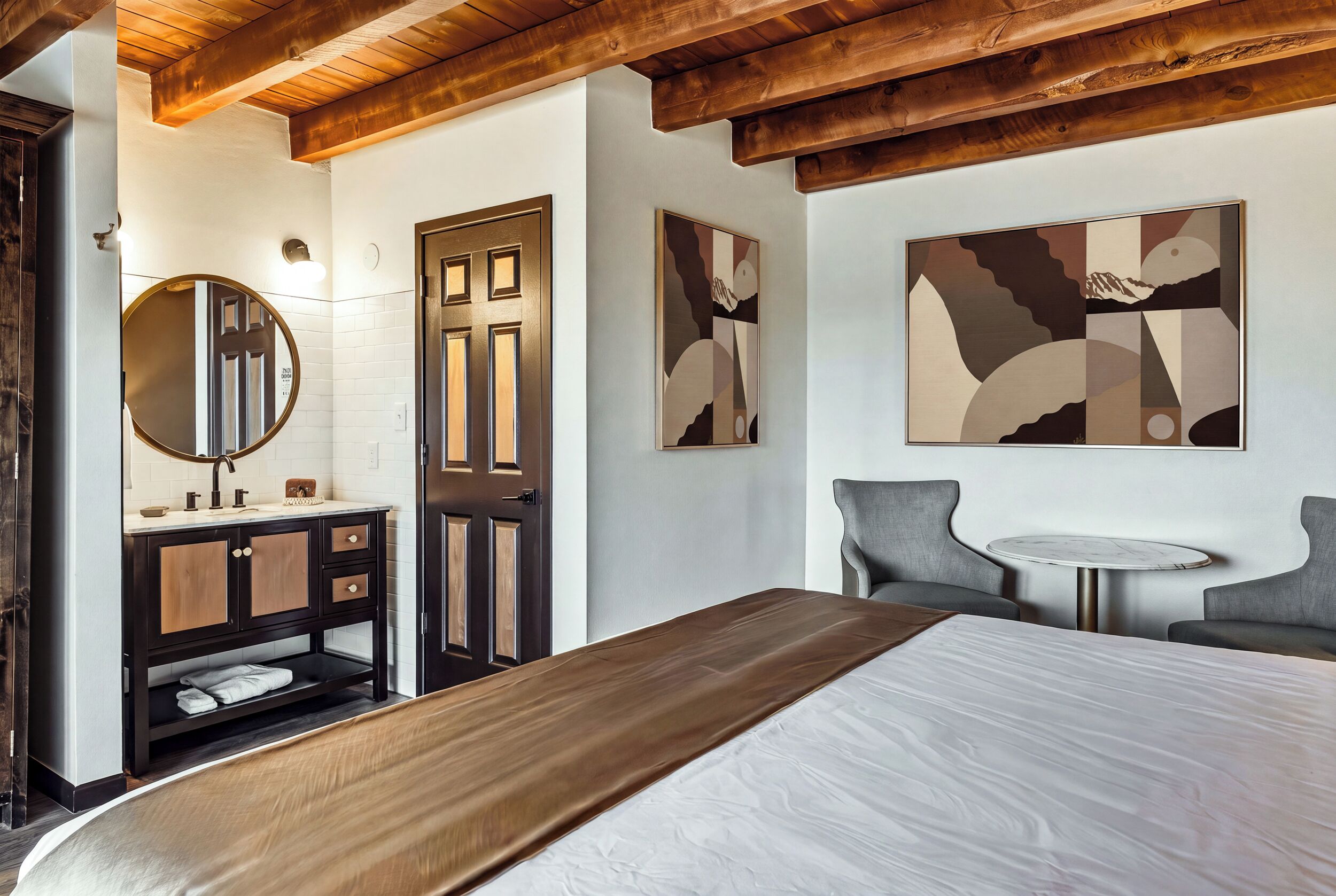 Ein modernes Schlafzimmer mit Holzboden, einem großen Bett, einem Nachttisch, einem Sessel und abstrakter Wandkunst.