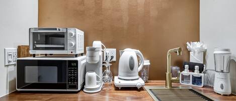 Eine Küchenzeile mit Mikrowelle, Kaffeemaschine, Wasserkocher und Mixer.