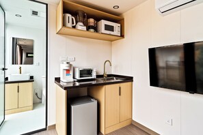 Een compacte keuken met een magnetron, broodrooster en spoelbak, een kleine koelkast en een aan de muur bevestigde televisie.