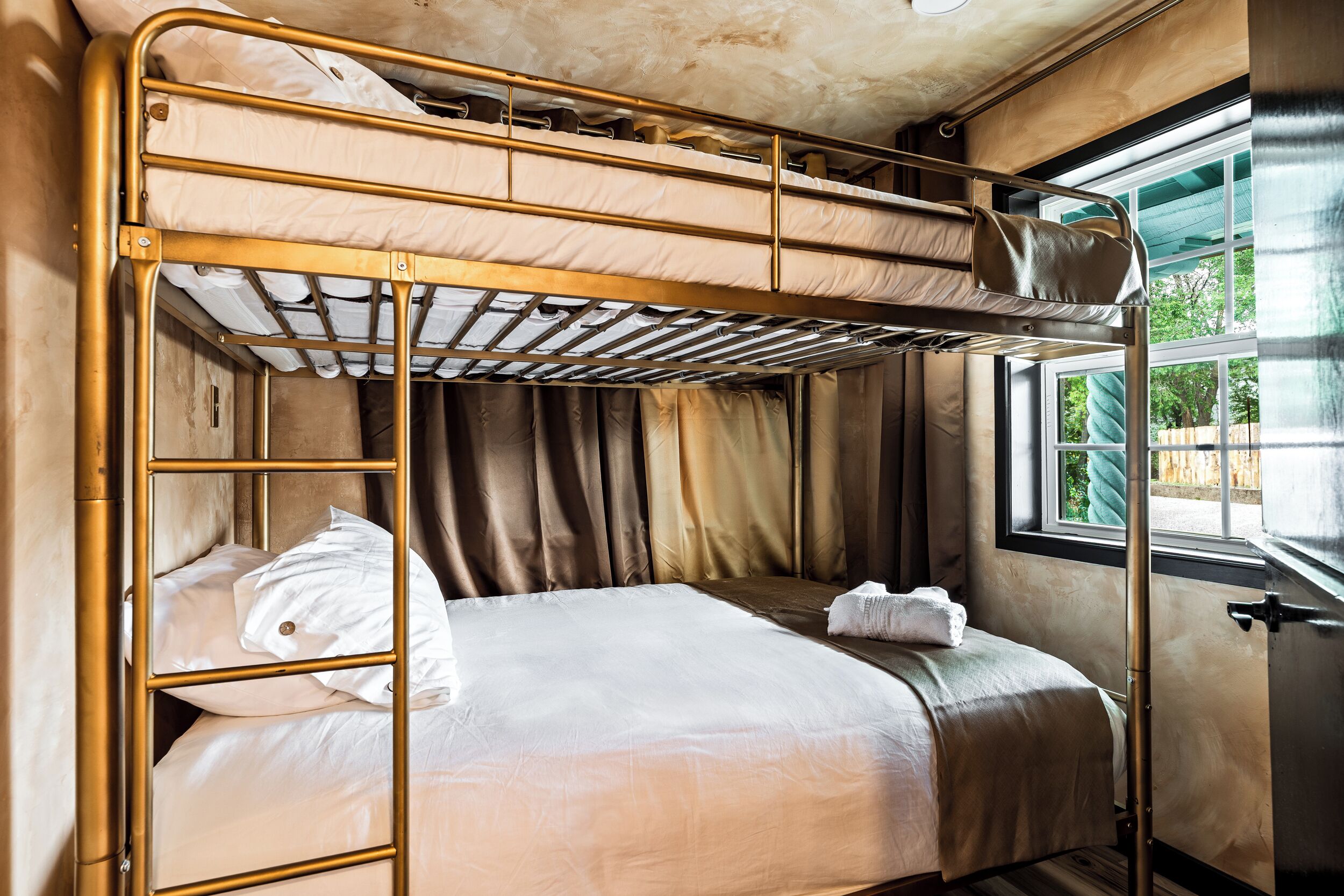 A bunk bed with a window, curtains, and a towel on the bed.