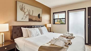 Ein Hotelzimmer mit einem großen Bett, zwei Nachttischlampen, einem gerahmten Kunstwerk über dem Bett und Blick durch das Fenster.