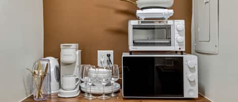 A kitchenette with a coffee maker, a microwave, a toaster, and a stack of pots and pans.