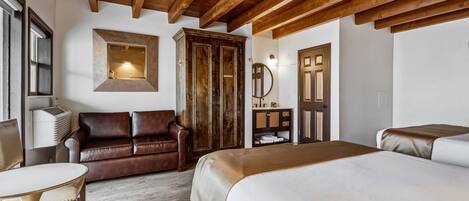 A hotel room with a wooden ceiling, a brown leather sofa, a bed with a white bedspread, a small round table, and a wardrobe.