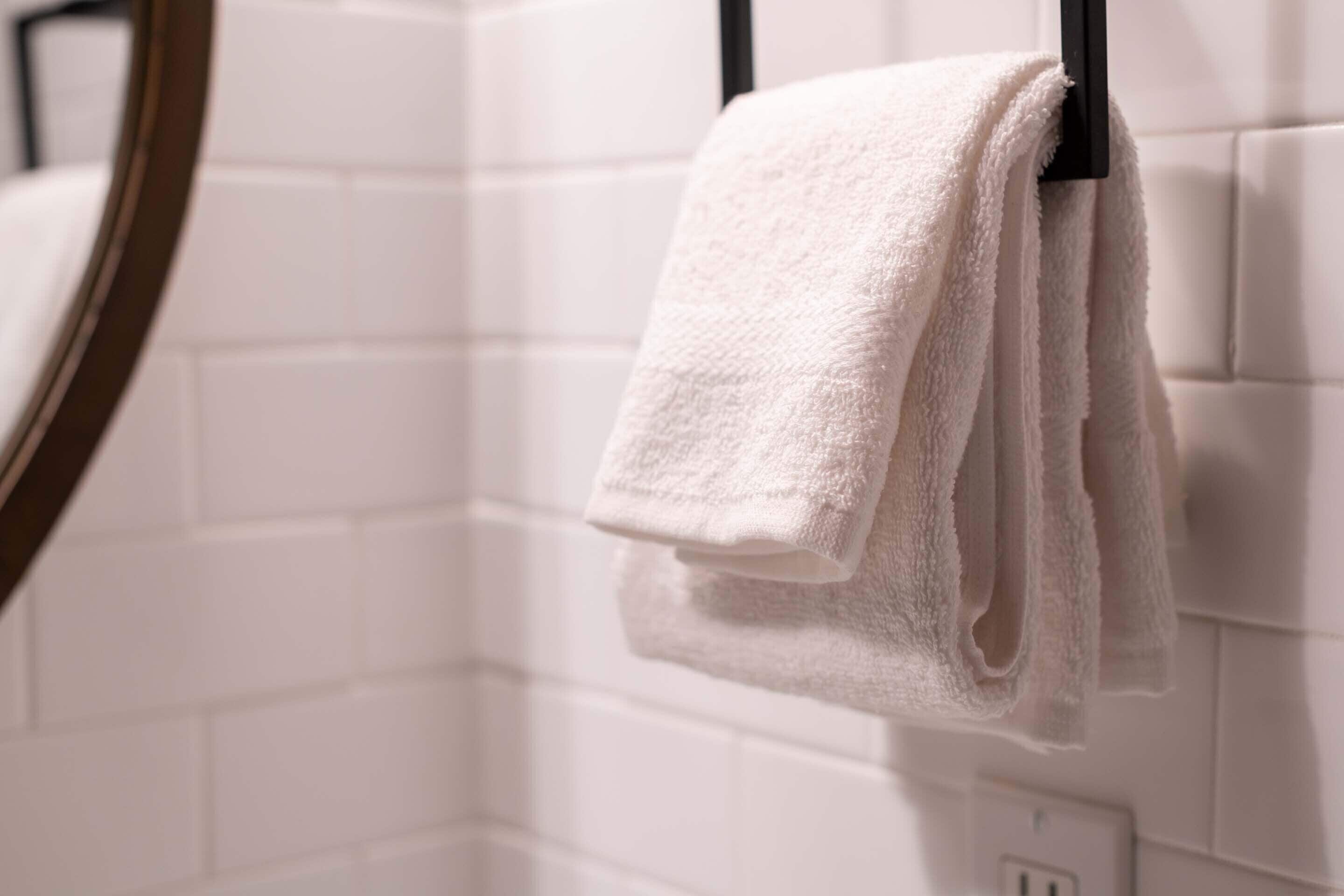 Una toalla blanca colgada en un perchero negro en un baño con paredes de azulejos blancos.