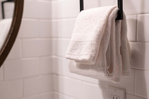 Een witte handdoek hangt aan een zwarte handdoekhouder in een badkamer met witte betegelde wanden.