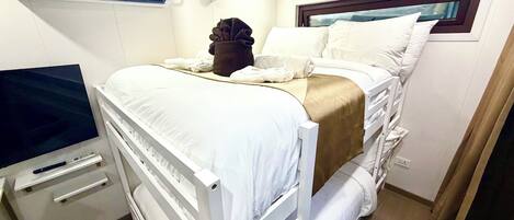 Una cama individual con ropa blanca, una mesita de noche con televisor de pantalla plana y una ventana con vistas.