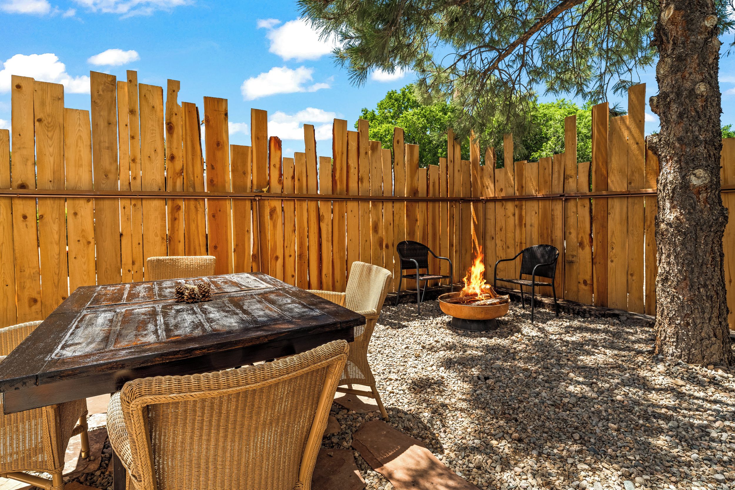 Eine Holzterrasse mit Tisch, Stühlen und einem Feuerkorb, sowie ein Baum.