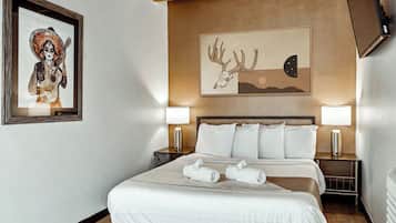Hotellihuone, jossa on sänky, kaksi yöpöytävalaisinta, seinällä taulu ja yöpöytä.