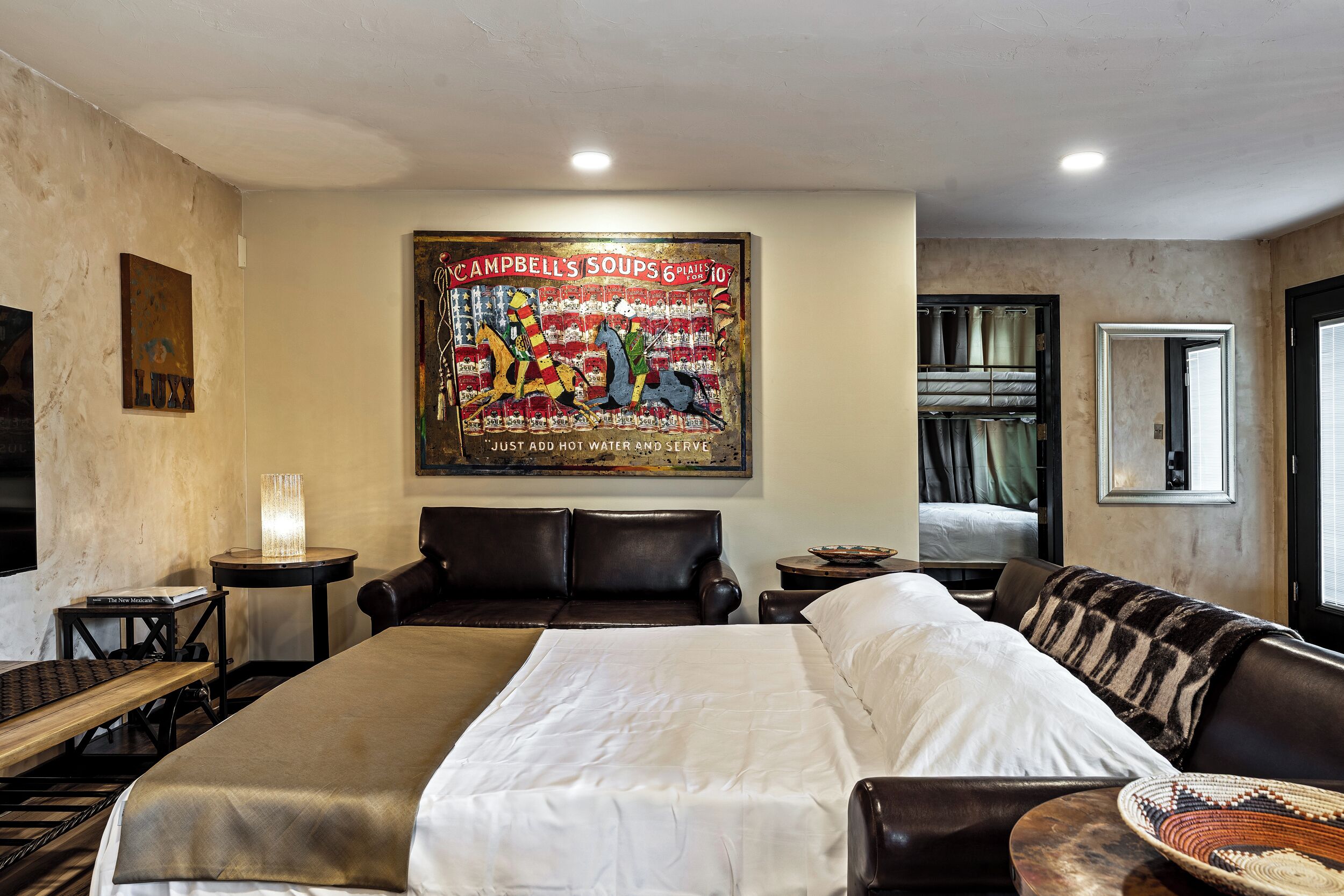 A hotel room with a large bed, a leather sofa, a small table with a lamp, and a wall-mounted painting.