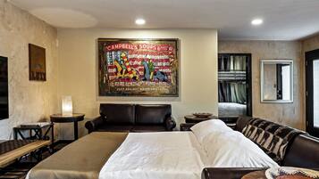 A hotel room with a large bed, a leather sofa, a small table with a lamp, and a wall-mounted painting.