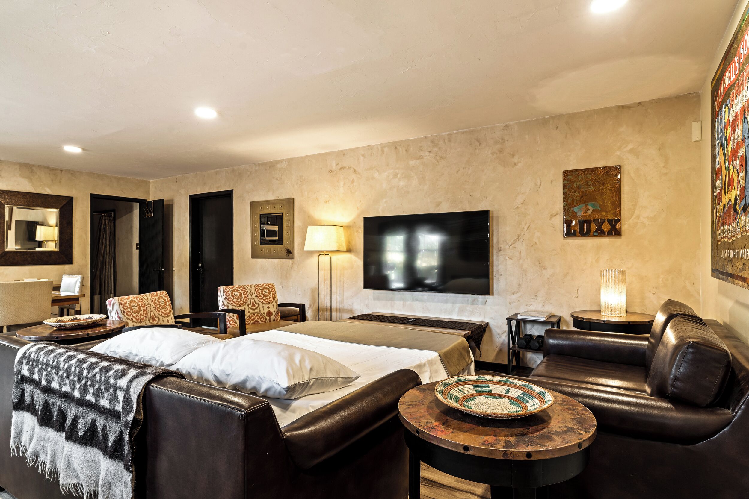 Habitación de hotel con cama, sofá, televisor, lámpara y un cuadro en la pared.